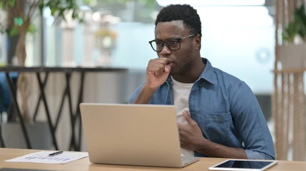 Africký muž kašel při použití notebooku v moderní kanceláři — Stock fotografie
