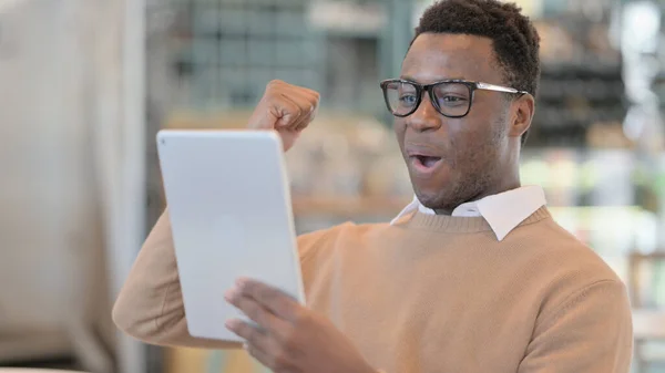 Africký muž šťastný za výsledky na digitální tabletu v kavárně — Stock fotografie