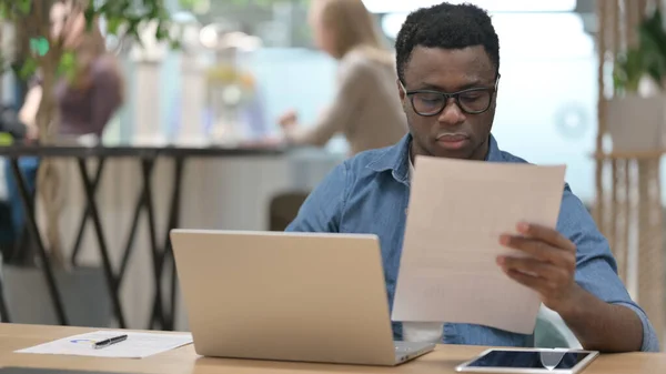 African Man Läsa dokument medan du arbetar på laptop — Stockfoto