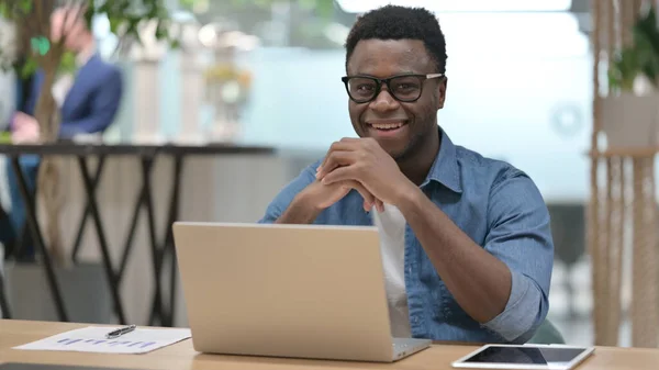 Afrikansk man ler mot kameran när du arbetar på laptop — Stockfoto