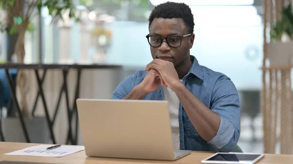 L'homme africain pense tout en utilisant un ordinateur portable dans le bureau moderne — Photo