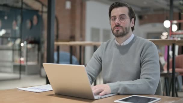 Jonge man toont duimen naar beneden ondertekenen tijdens het gebruik van laptop op het werk — Stockvideo