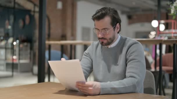 Giovane uomo che legge documenti mentre è seduto in ufficio — Video Stock