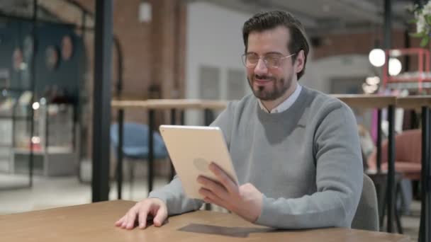Молодий чоловік робить відеодзвінок на планшеті в офісі — стокове відео