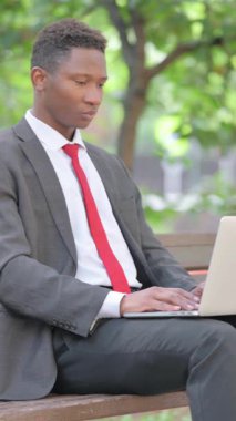 Şok olmuş Afrikalı iş adamı kucağında dizüstü bilgisayarla kameraya bakıyor.