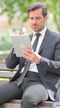 Orta yaşlı işadamı Bench 'te otururken dijital tablet kullanıyor.