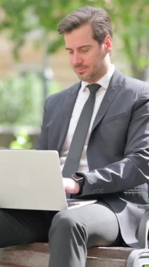 Orta yaşlı iş adamı Bench 'te otururken dizüstü bilgisayarda çalışıyor.