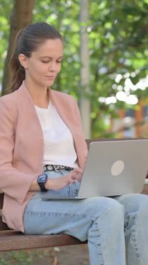 Park 'ta otururken dizüstü bilgisayarda çalışan genç kadın.