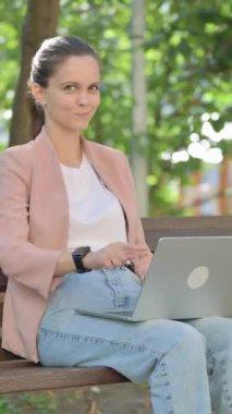 Dışarıdaki Laptop 'u kullanırken kamerayı gösteren genç kadın.