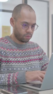 Laptop 'ta çalışırken kameraya bakan İspanyol genç adam, dikey video