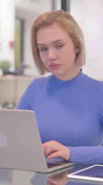 Ofiste dizüstü bilgisayarda çalışırken kameraya bakan genç kadın, dikey video