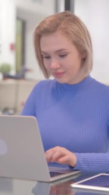 Ofiste dizüstü bilgisayarda çalışırken kameraya gülümseyen genç kadın, dikey video