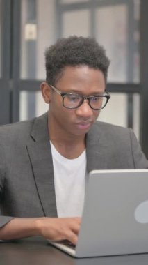 Ofiste dizüstü bilgisayarla çalışırken kameraya bakan dikey, Afrikalı Amerikalı Adam