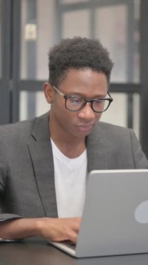 Ofiste dizüstü bilgisayarda çalışırken kameraya gülümseyen dikey, Afrikalı Amerikalı adam