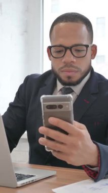Karışık Yarış İşadamı Laptop ve Akıllı Telefon Üzerinde Çalışıyor, dikey video
