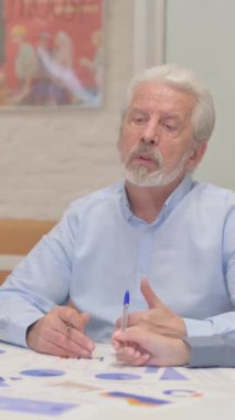 Yaşlı adam evrak işi yaparken takım arkadaşlarıyla konuşuyor, dikey video