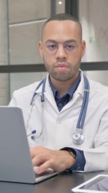 Laptop ve dikey video üzerinde çalışırken İspanyol Doktor Kameraya Bakıyor