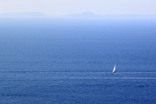 Velero blanco solitario en el espacio marítimo entre olas azules y horizonte lejano . — Foto de Stock
