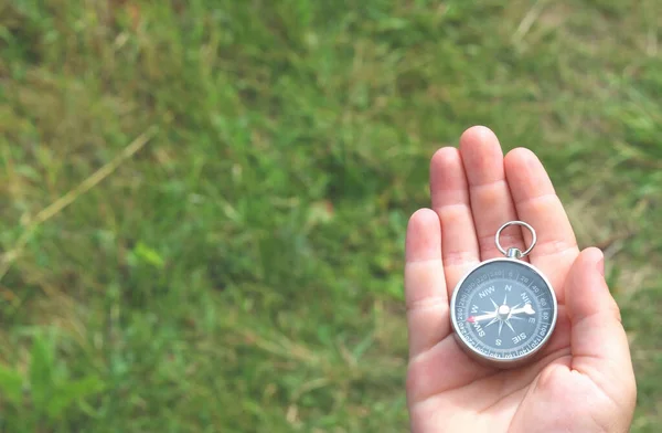 Old classic navigation compass in hand on natural background as symbol of tourism with compass, travel with compass and outdoor activities with compass