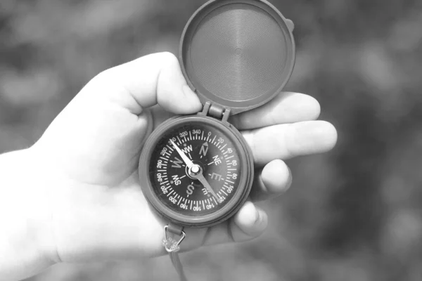 Old classic navigation compass in hand on natural background as symbol of tourism with compass, travel with compass and outdoor activities with compass