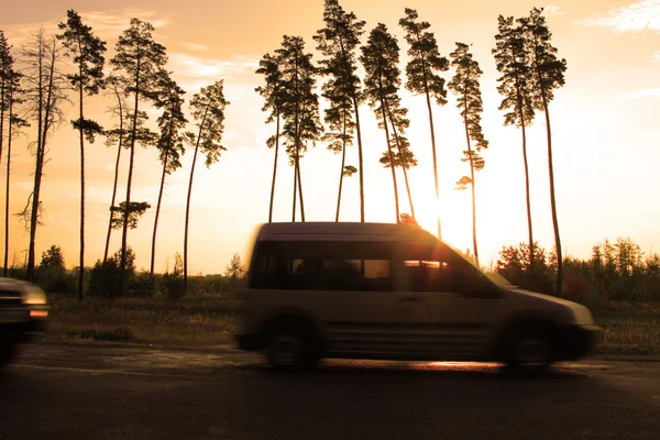 Niewyraźne drogi i samochód na tle piękny zachód słońca i drzew — Zdjęcie stockowe
