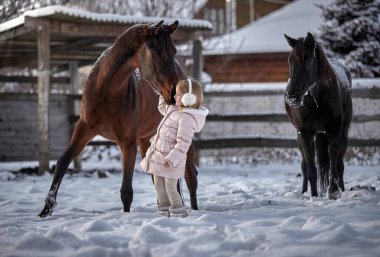 Güzel küçük kız kışın bir at yanında yürür.