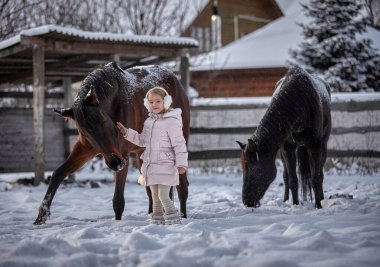 Güzel küçük kız kışın bir at yanında yürür.