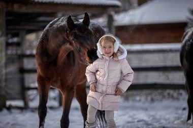 Güzel küçük kız kışın bir at yanında yürür.