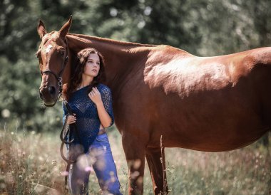 Güzel kıvırcık saçlı bir kız kırmızı bir atın yanında duruyor.
