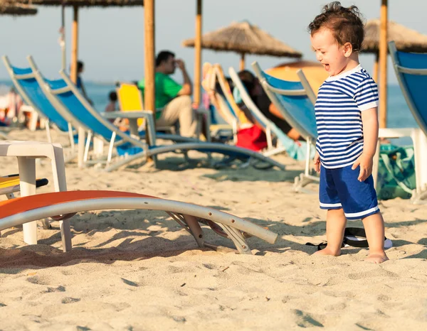 Toddler dressed as a sailor standing on a beach and crying with — Stock Photo, Image
