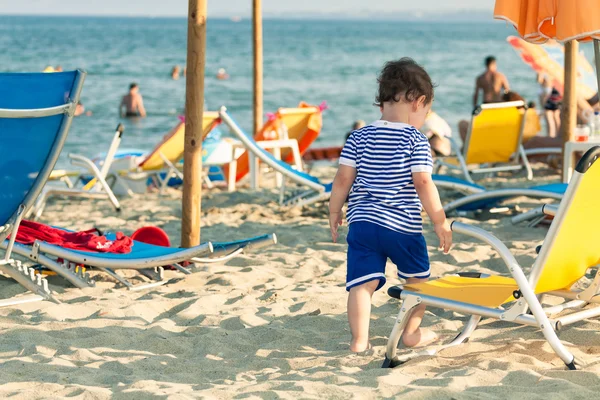Toddler dressed as a sailor standing near a beach chair with oth — Stock Photo, Image