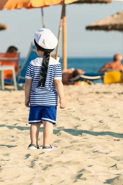 Toddler dressed as a sailor standing on a beach, looking around — Stock Photo, Image