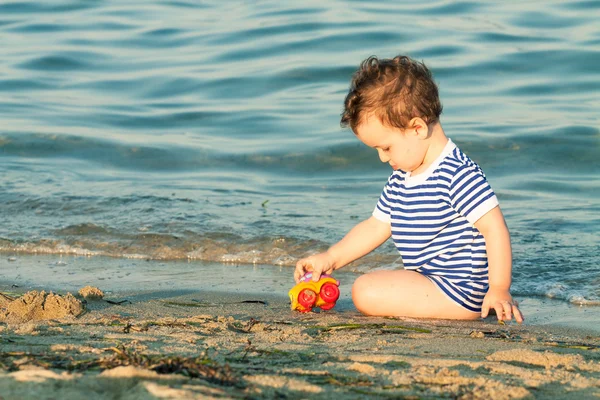 Niño pequeño con camisa marinera sentado y jugando en el borde de la — Foto de Stock