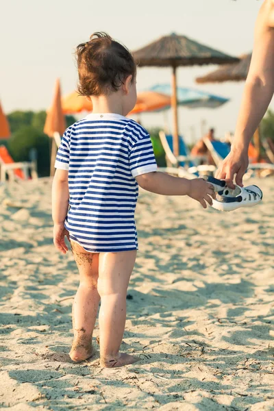 Kvinna hand ger flip flops till ett litet barn med sjöman skjorta på en — Stockfoto