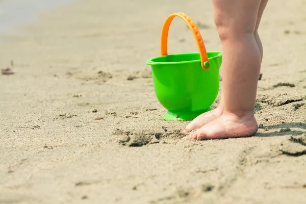 Gros plan des pieds d'un tout-petit et d'un seau sur une plage. Photo avec u — Photo