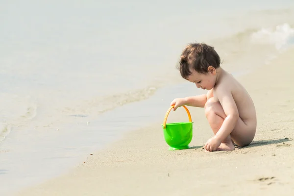 Bébé mignon et un seau à jouets sur une plage au bord de la mer — Photo