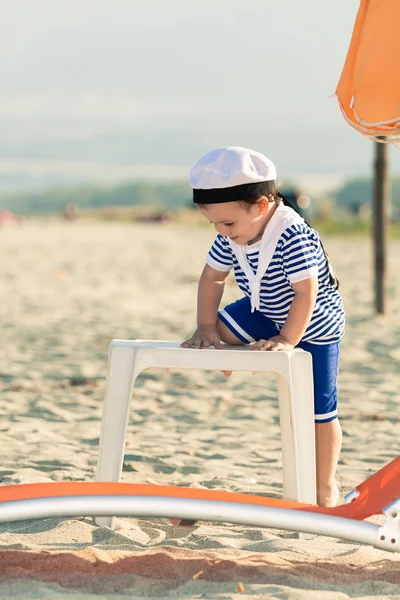 Playful toddler dressed as a sailor standing on a beach and clim — Stock Photo, Image