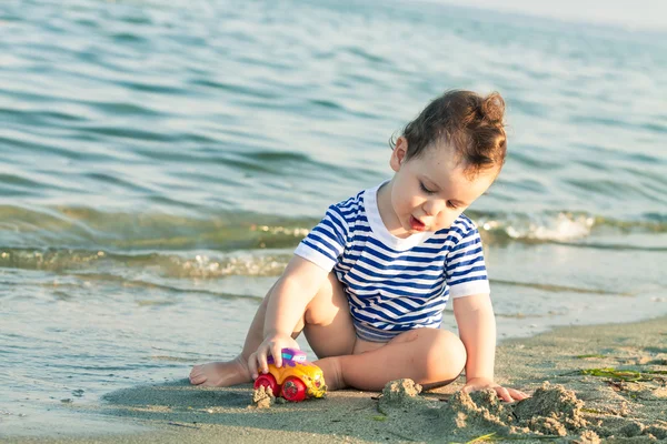 Playful toddler with sailor shirt playing with a car at the edge — Stock Photo, Image