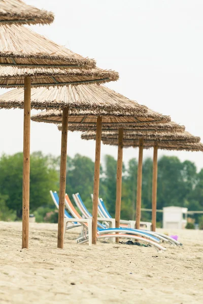 Fila di ombrelloni di paglia e lettini in spiaggia. Foto con untradi — Foto Stock