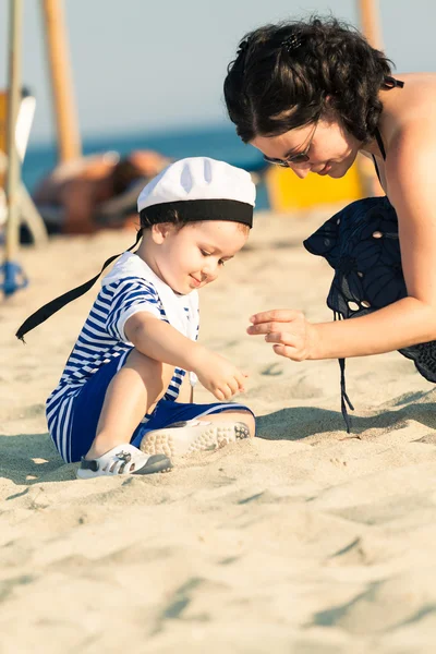 Dolce bambino sorridente vestito da marinaio seduto su una spiaggia e — Foto Stock