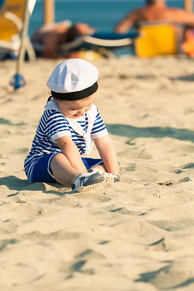 Zoete lachende peuter verkleed als een zeeman zittend op een strand en — Stockfoto