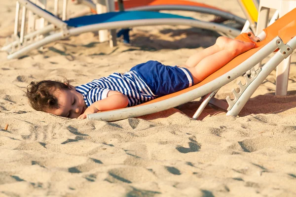 Söt liten knatte klädd som en sjöman liggande från en topp av en solbädd o — Stockfoto