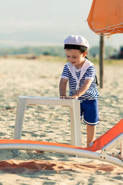 Sweet toddler dressed as a sailor standing on a beach near a pla — Stock Photo, Image