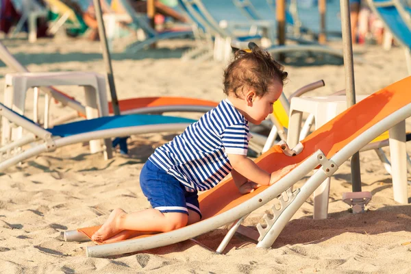 Toddler dressed as a sailor climbing on a tilted sunbed on a bea Stock Photo