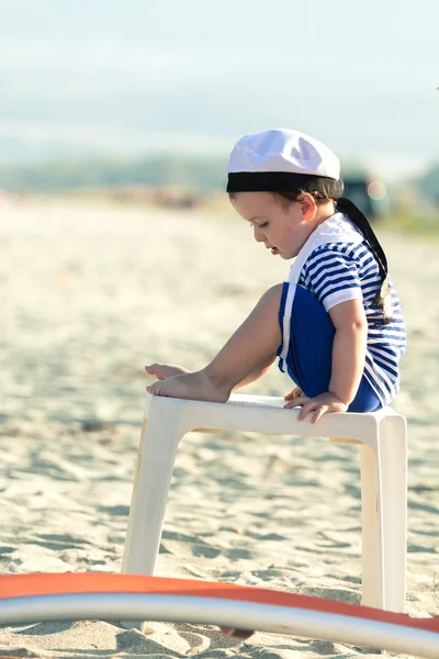 Sweet toddler dressed as a sailor sitting on a plastic table on Stock Photo