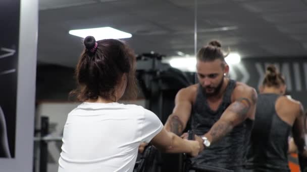 Gym Lesson with a young funny trainer man A beginner woman shakes her back and arms on the simulator — Stock Footage Gym Lesson with a young funny trainer man A beginner woman shakes her back and arms on the simulator Royalty Free Stock Footage