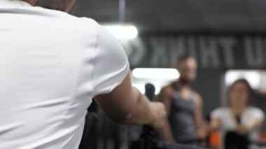 Genç ve komik bir antrenörle beden eğitimi dersi. Acemi bir kadın simülatörde sırtını ve kollarını sallıyor.