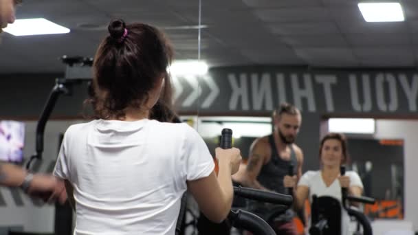 Gym Lesson with a young funny trainer man A beginner woman shakes her back and arms on the simulator — Stock Footage Gym Lesson with a young funny trainer man A beginner woman shakes her back and arms on the simulator Stock Footage