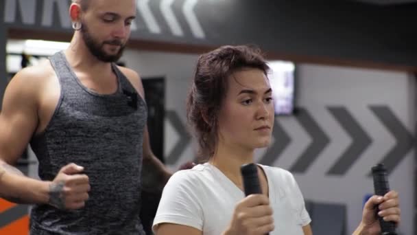 Gym Lesson with a young funny trainer man A beginner woman shakes her back and arms on the simulator — Stock Footage Gym Lesson with a young funny trainer man A beginner woman shakes her back and arms on the simulator Royalty Free Stock Video