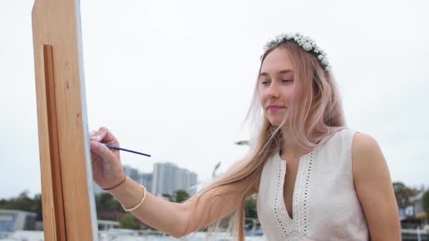 Jovem loira pinta quadro na praia Ao ar livre Contra o fundo de gaivotas voadoras — Vídeo de Stock